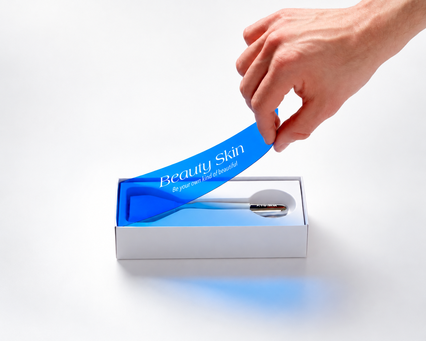 Hand lifting a blue transparent cover from a white cosmetic rigid box, revealing a cosmetic item in a fitted white insert.