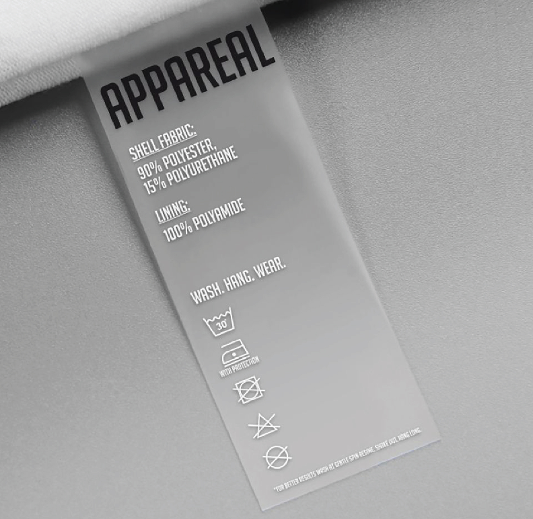 Grey clothing care label with black branding, white fabric composition text and washing care symbols.